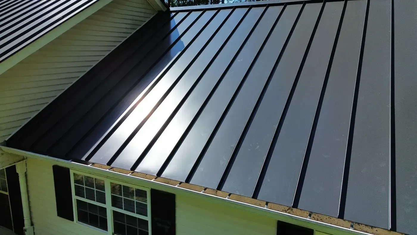 Close view of a charcoal standing seam metal roof, sun catching the raised seams above the eave