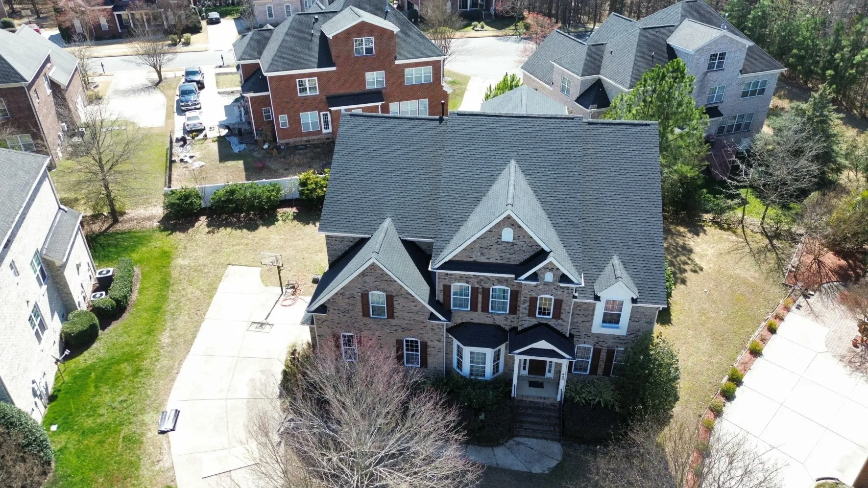 Aerial view of a two-story brick home with a dark gray architectural shingle roof in Cary, NC