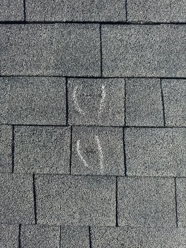 Storm-damaged shingles showing impact marks and cracking from hail
