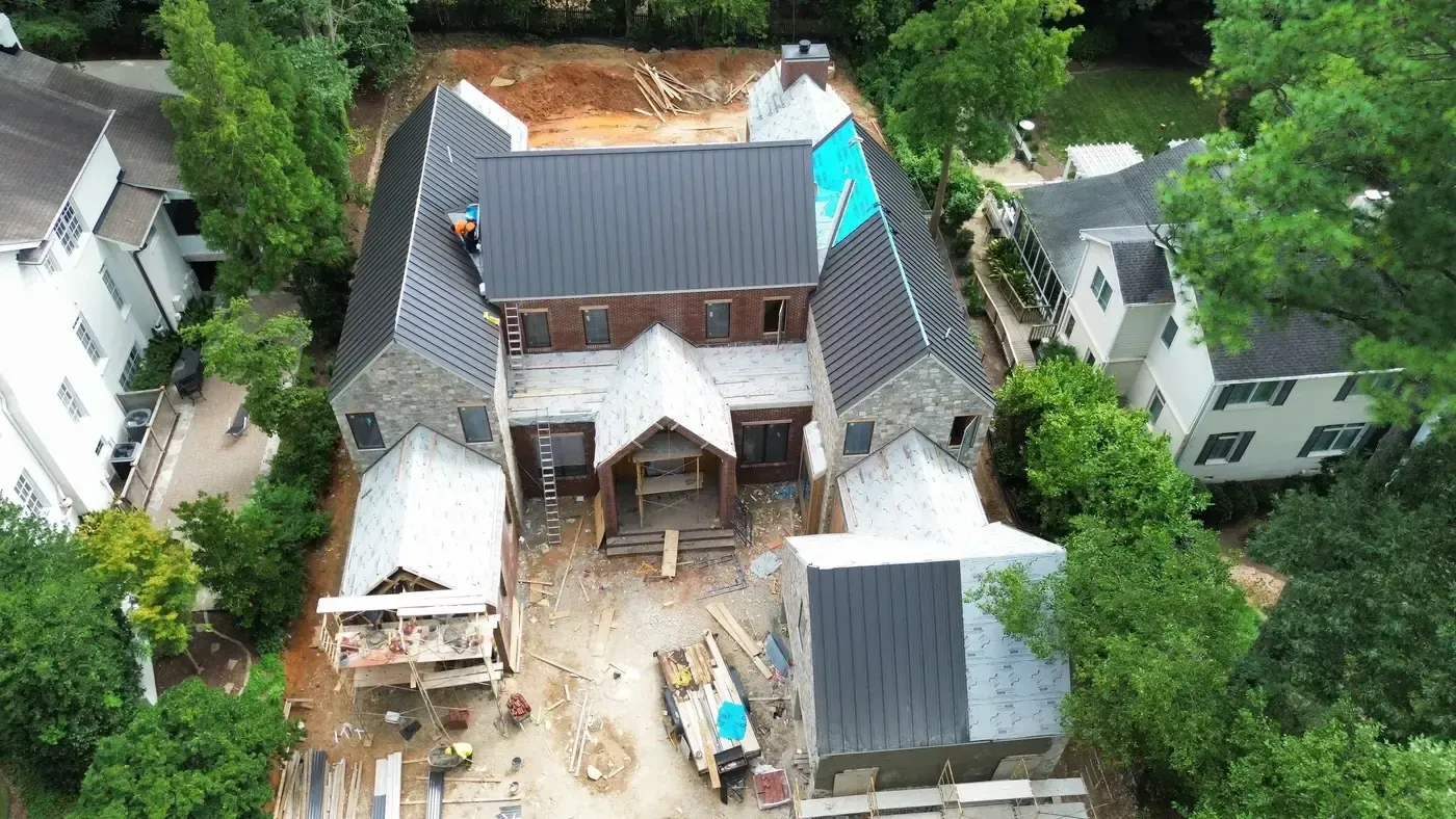 Large custom home under construction in Raleigh, NC with dark standing seam metal going on across multiple gables
